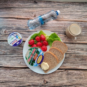 Zdjęcie przedstawia dietę z ograniczeniem łatwoprzyswajalnych węglowodanów Chleb Graham Masło extra Serek wiejski ziarnisty Kawa zbożowa z mlekiem Jogurt naturalny Woda źródlana Sałata zielona Pomidorki koktajlowe